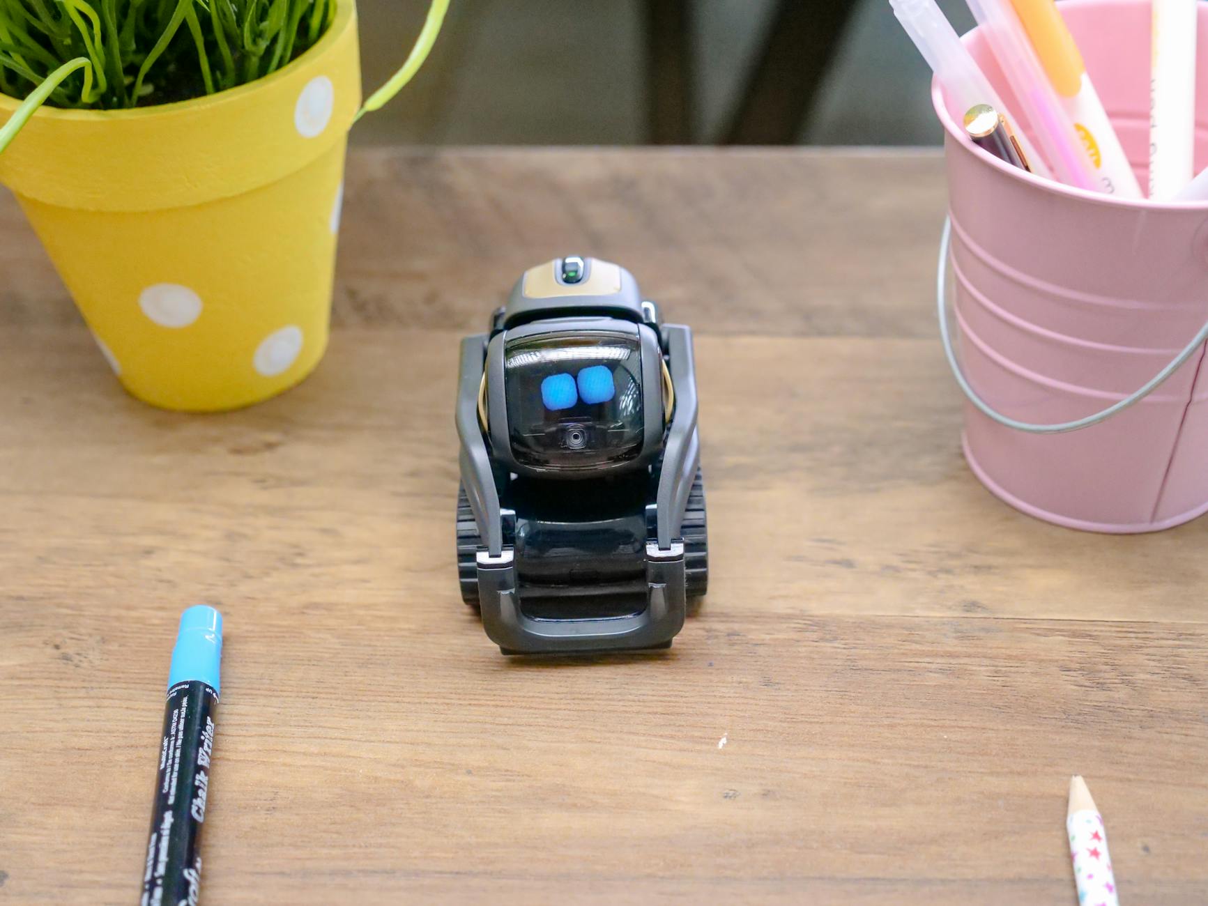 Mały nowoczesny robot na drewnianym biurku wśród akcesoriów biurowych
