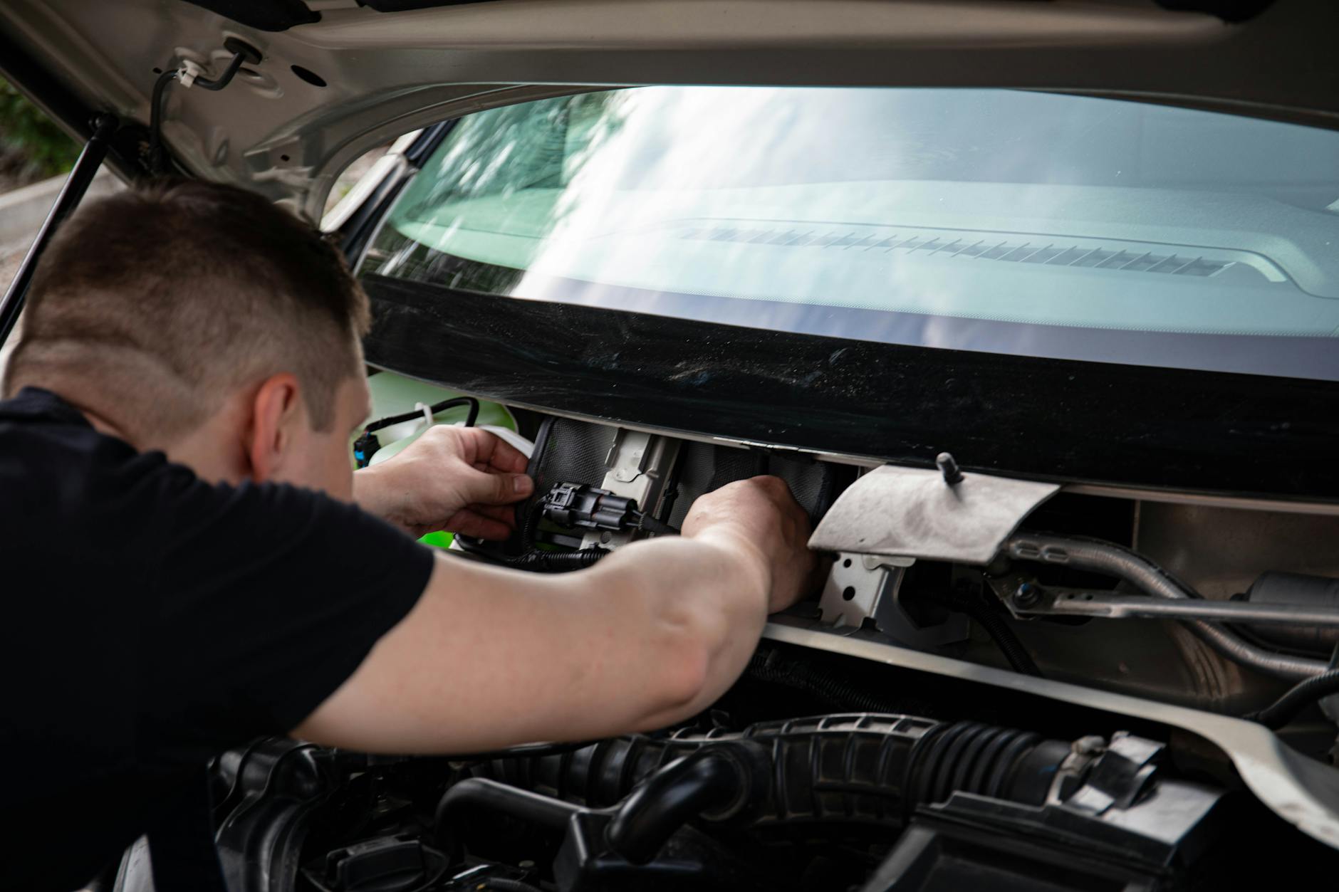 Mechanik naprawiający instalację elektryczną w komorze silnika auta