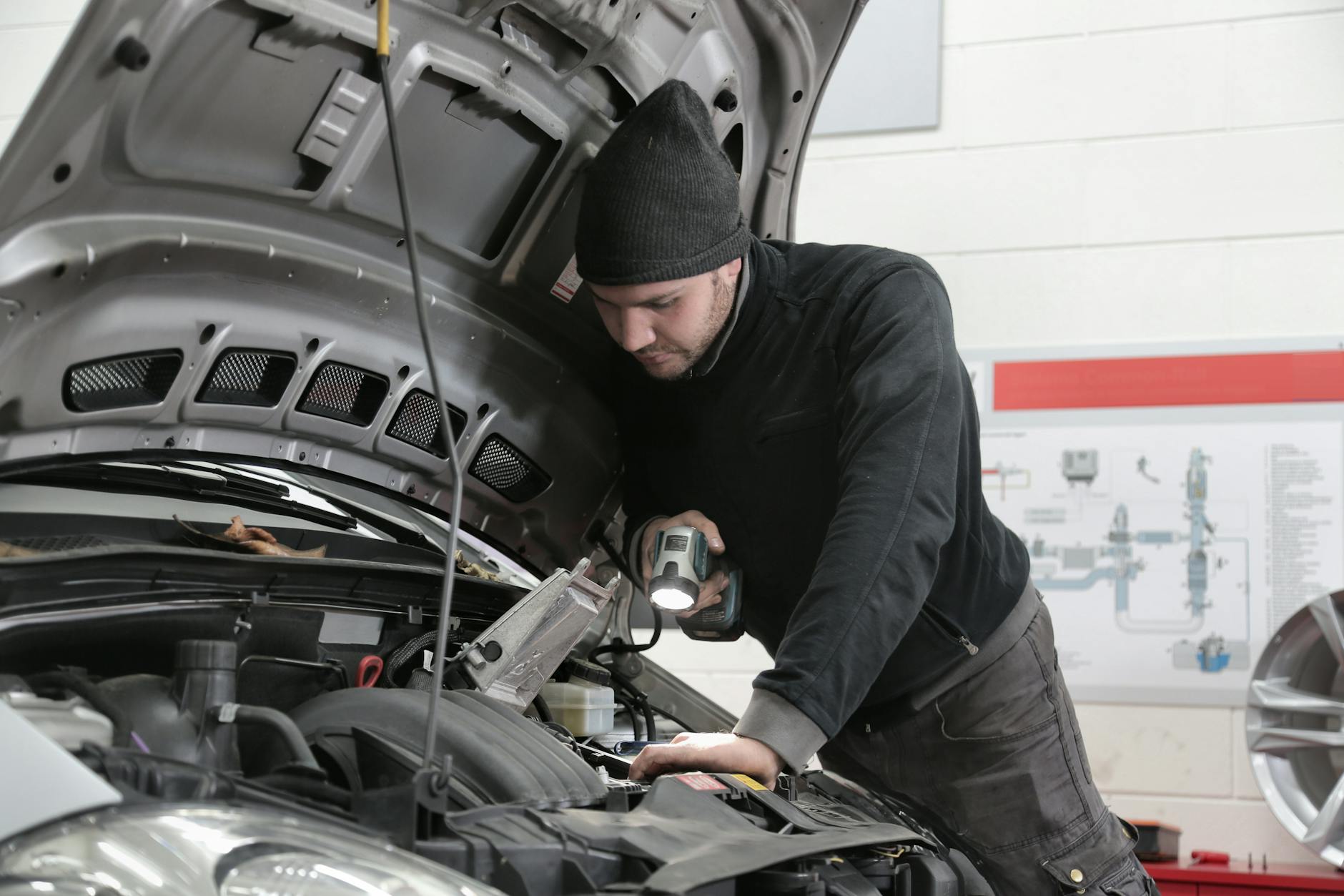 Mechanik z latarką dokładnie ogląda silnik Mazdy 5 w warsztacie