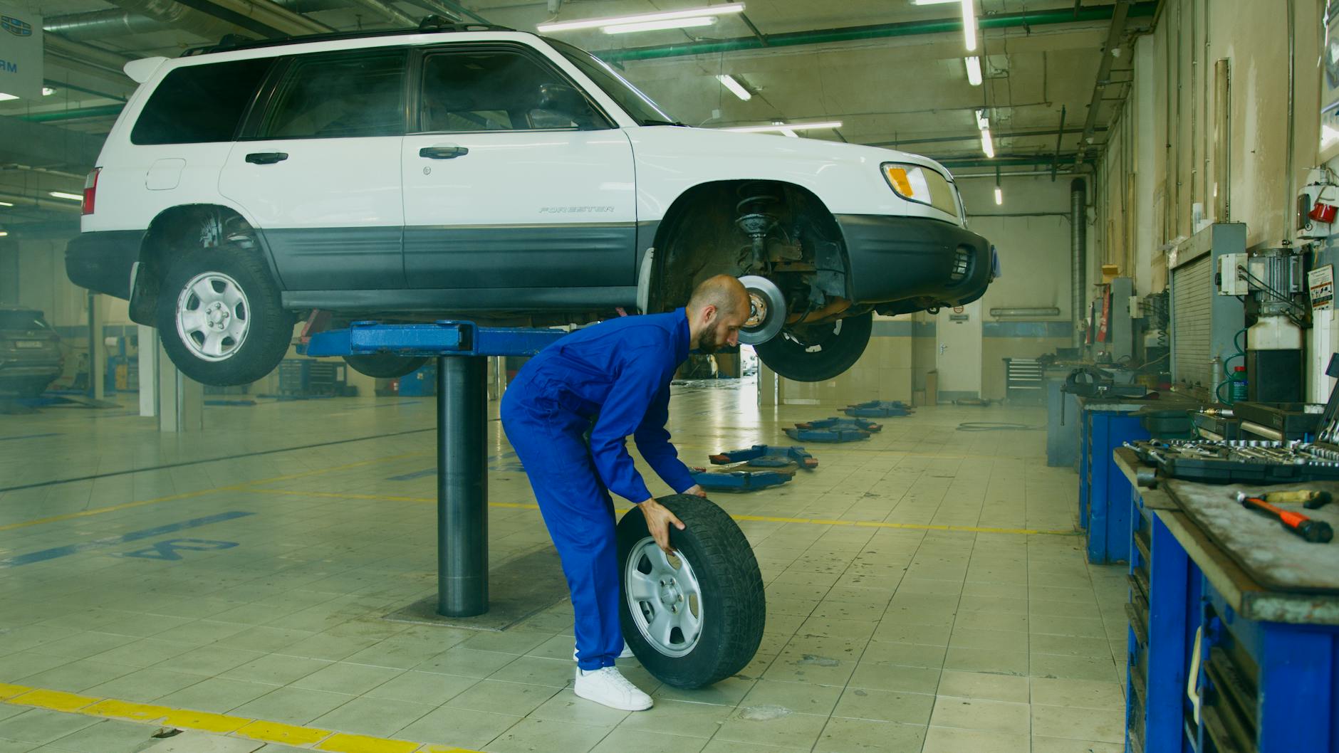 Jak wymienić sprężynę zawieszenia w Mazdzie 5 bezpiecznie i bez uszkodzeń amortyzatora Mechanik przy podniesionym aucie w warsztacie podczas wymiany koła